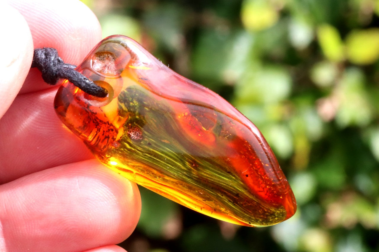 Amber amulet style pendant held in a hand with a blurred green background