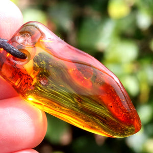 Amber amulet style pendant held in a hand with a blurred green background