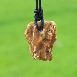 A natural raw amber stone pendant with white veining, threaded on a black cord, set against a vibrant green blurred background.