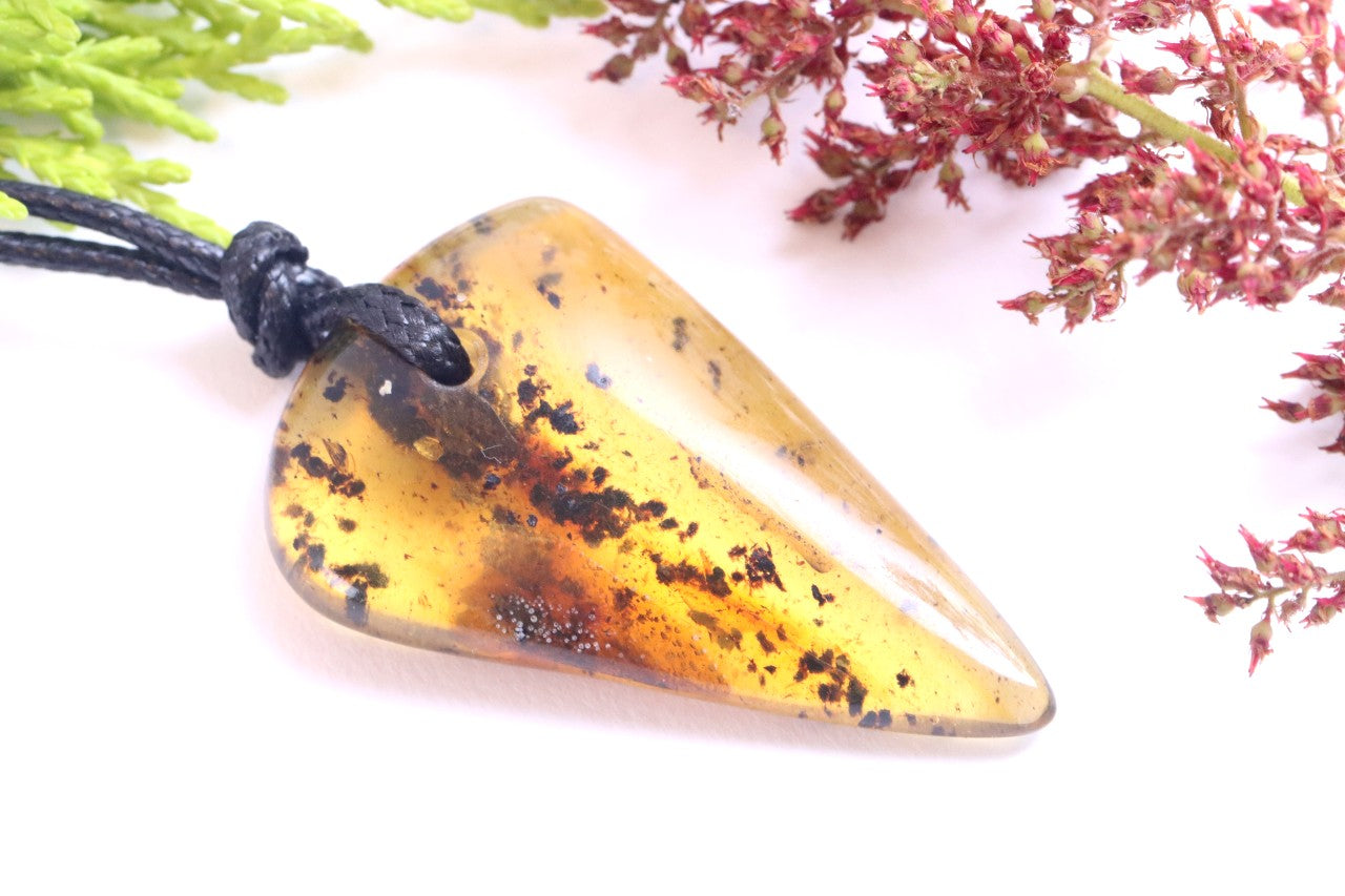 Triangular amber pendant on a white background with green and red leaves.