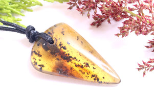 Triangular amber pendant on a white background with green and red leaves.