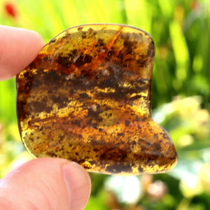 Hand holding a heart-shaped piece of amber with a blurred natural background