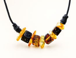 A close-up of a necklace with a black cord and a row of polished amber beads in various shapes and colors, including yellow, orange, and dark brown, on a white background.