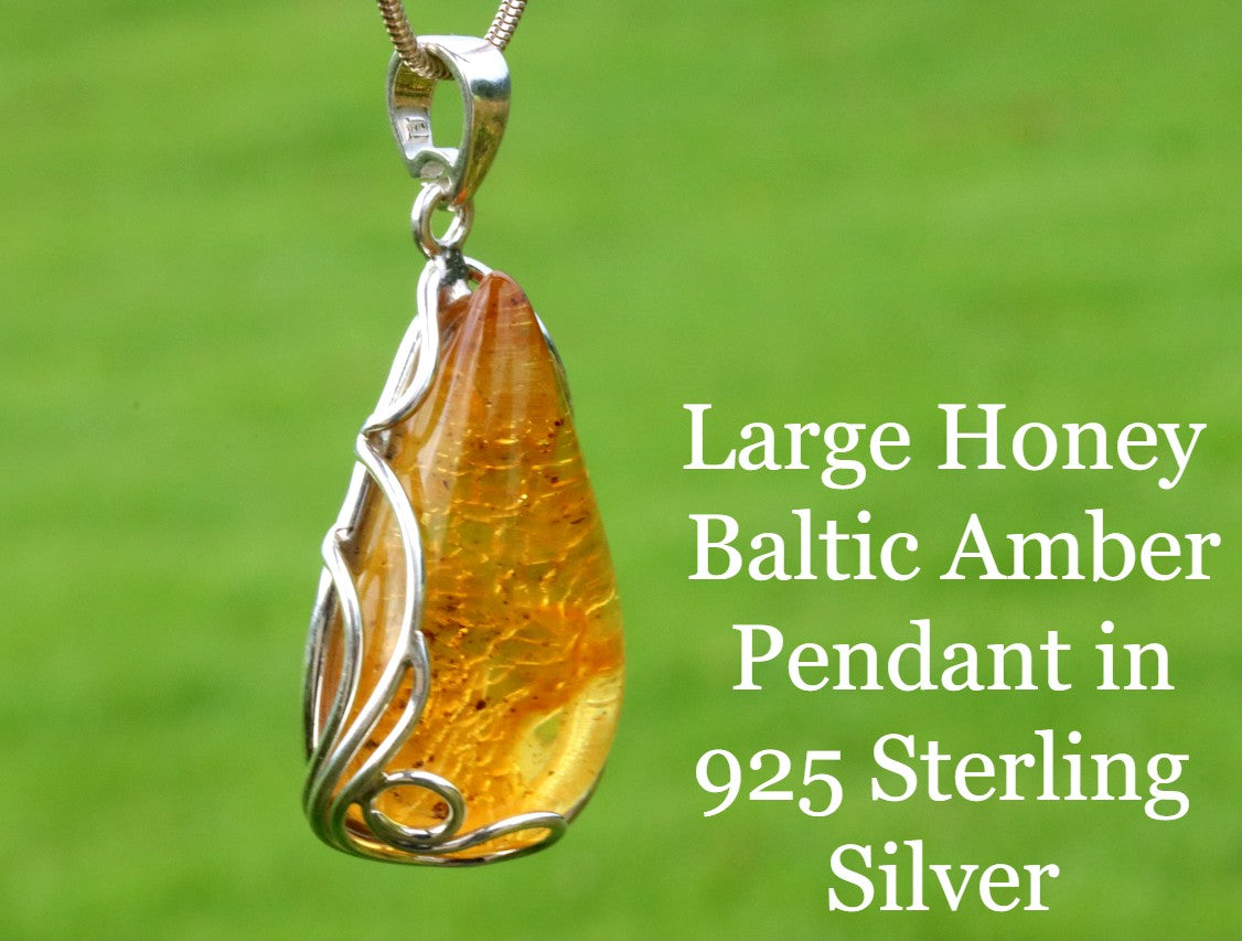 Large honey Baltic Amber pendant in 925 Sterling Silver on a green background