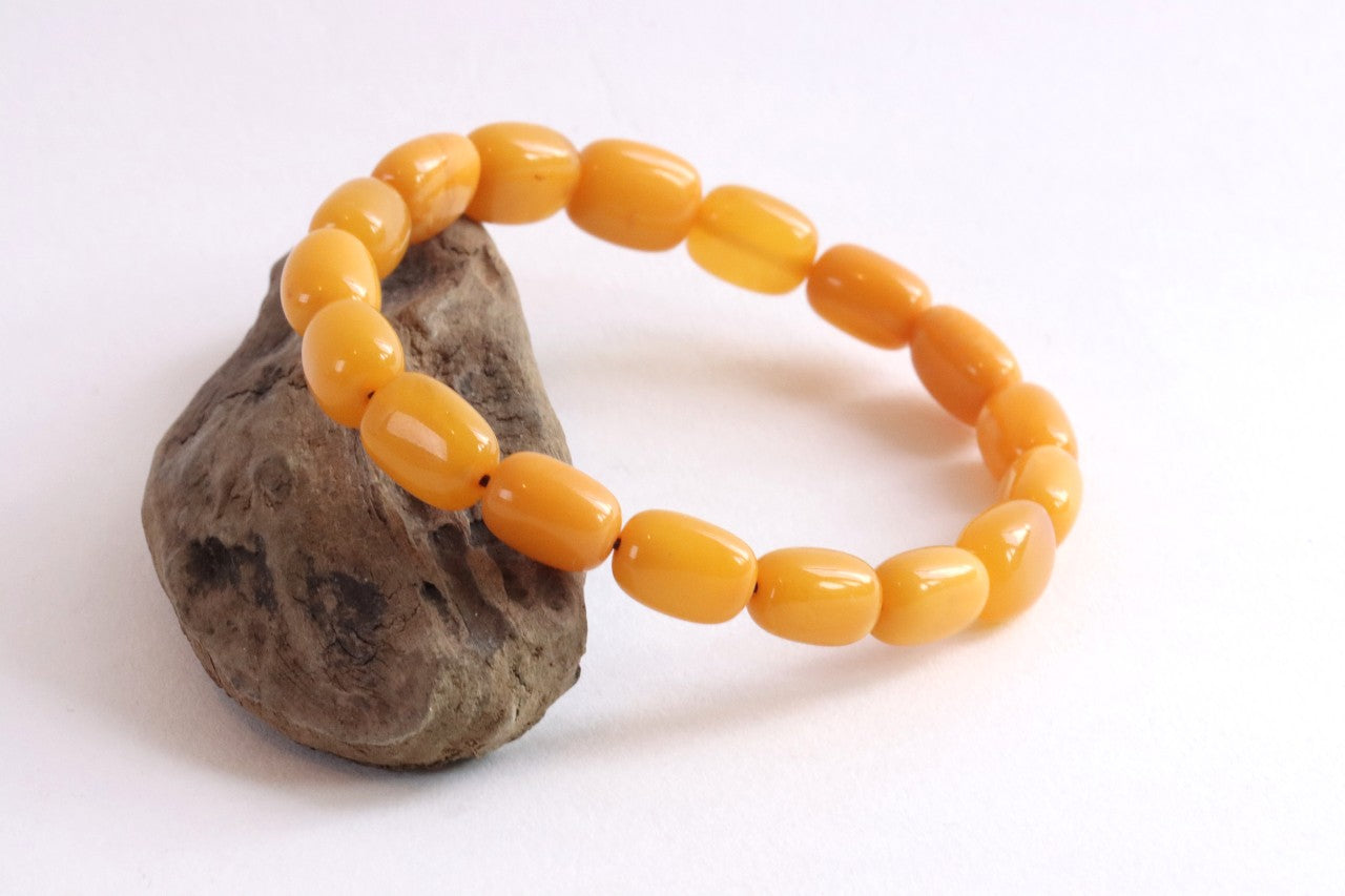 A beaded stretch bracelet made of glossy, rounded amber-yellow beads, displayed on a small textured brown stone against a plain white background.