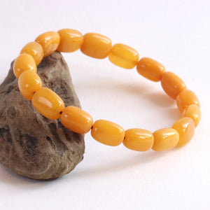 A beaded stretch bracelet made of glossy, rounded amber-yellow beads, displayed on a small textured brown stone against a plain white background.