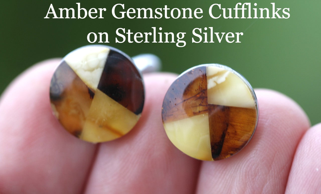 A pair of circle-shaped cufflinks made of Baltic amber gemstones set in sterling silver, held between fingers.