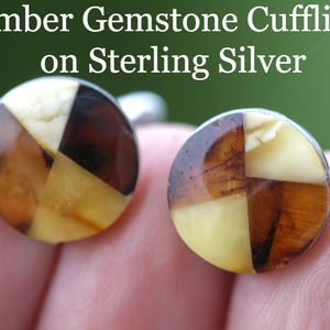 A pair of circle-shaped cufflinks made of Baltic amber gemstones set in sterling silver, held between fingers.