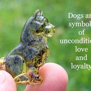 A small, hand-carved amber figurine of a dog, held in someone's hand, with a green and yellow background.