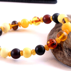 Multicolored beaded bracelet on a white surface with a piece of wood.