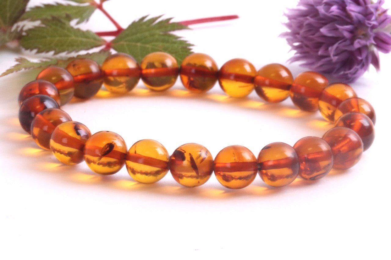 Beaded bracelet with amber-like beads on a white background with green leaves and a purple flower.