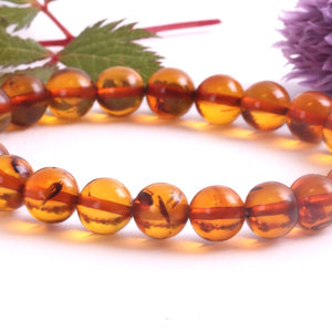 Beaded bracelet with amber-like beads on a white background with green leaves and a purple flower.