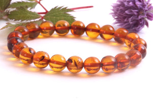 Beaded bracelet with amber-like beads on a white background with green leaves and a purple flower.