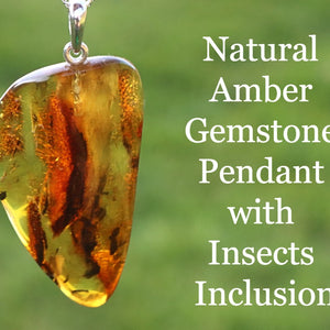 A teardrop-shaped natural amber gemstone pendant with insect inclusion, suspended by a silver loop, against an outdoor background.
