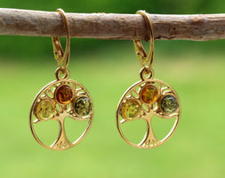 Gold earrings with embedded stones on a branch against a green background