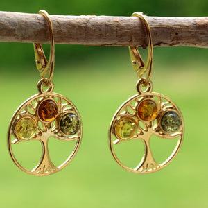Gold earrings with embedded stones on a branch against a green background