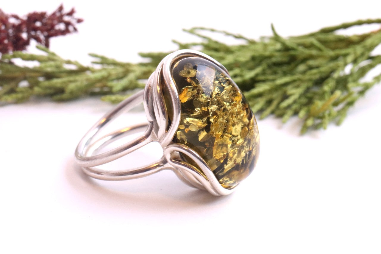 Silver ring with a large amber stone against a white background with greenery.