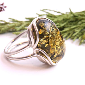 Silver ring with a large amber stone against a white background with greenery.