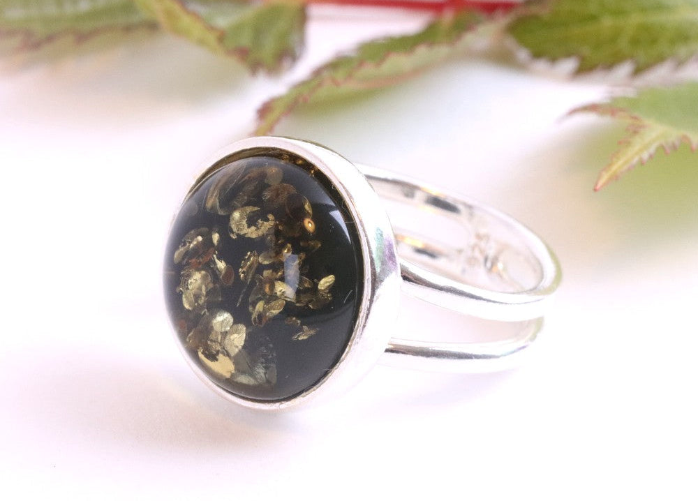 Silver ring with a black stone and gold flecks on a white background