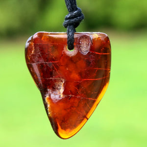 Heart-shaped amber pendant on a cord against a blurred green background
