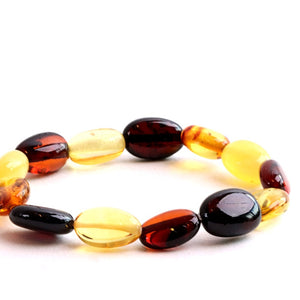 A beaded stretch bracelet made of polished oval amber-like beads in translucent yellow, deep amber-brown, and glossy black, photographed on a clean white background.