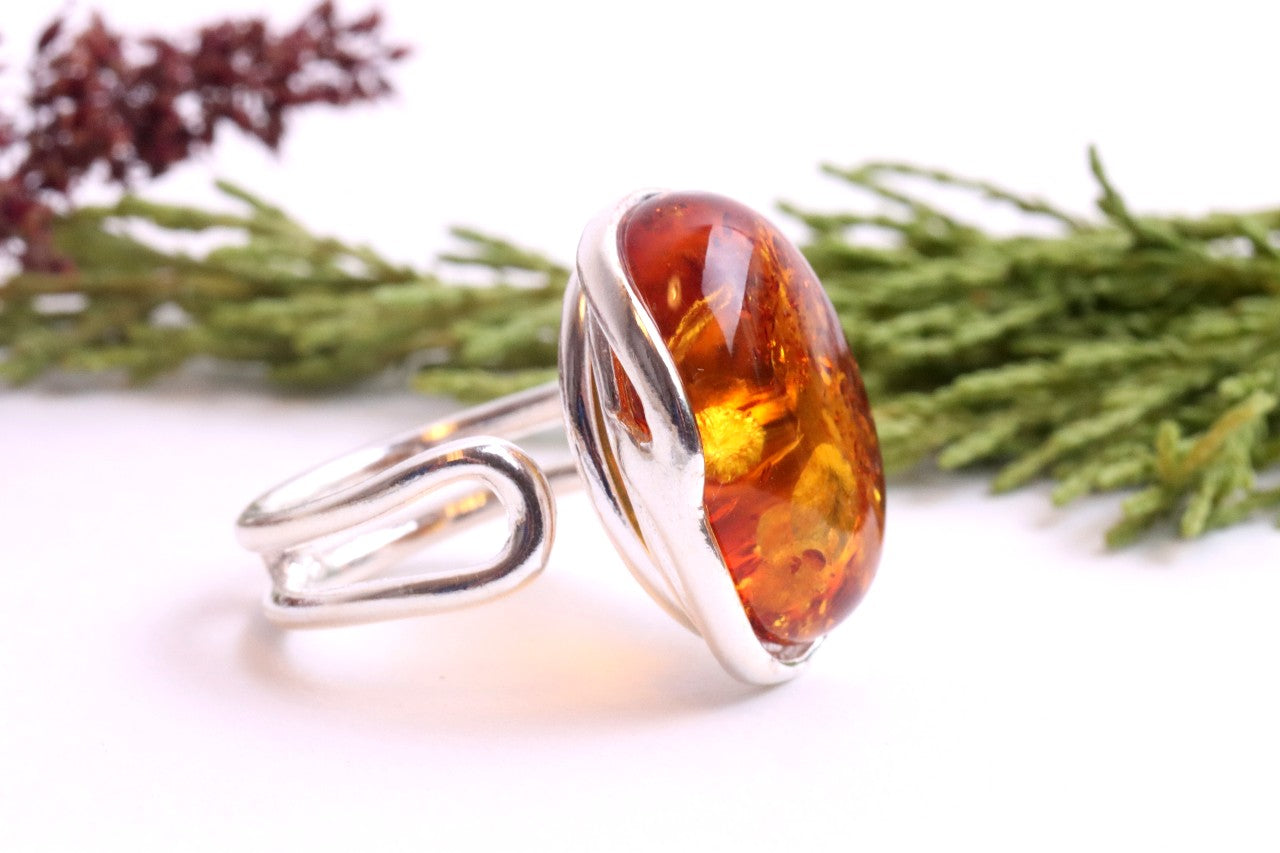 Silver ring with a large amber stone on a white background with green foliage.