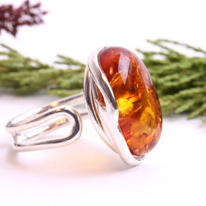Silver ring with a large amber stone on a white background with green foliage.