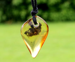 Teardrop-shaped amber pendant on a string against a blurred green background