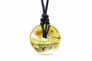A round translucent amber pendant necklace with a black cord, featuring natural inclusions and a polished finish, shown against a plain white background.