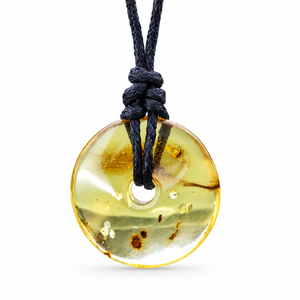 A round translucent amber pendant necklace with a black cord, featuring natural inclusions and a polished finish, shown against a plain white background.