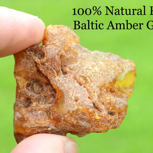 Raw Baltic Amber gem held between fingers with green background and text overlay