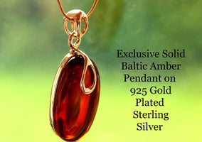 Red Baltic Amber Pendant on 925 Gold Plated Sterling Silver against a blurred green background