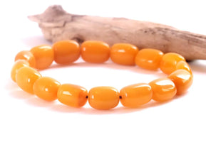 A beaded stretch bracelet made of glossy, rounded orange-yellow beads, displayed on a white surface with a piece of driftwood in the background.