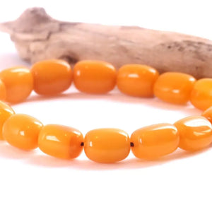 A beaded stretch bracelet made of glossy, rounded orange-yellow beads, displayed on a white surface with a piece of driftwood in the background.