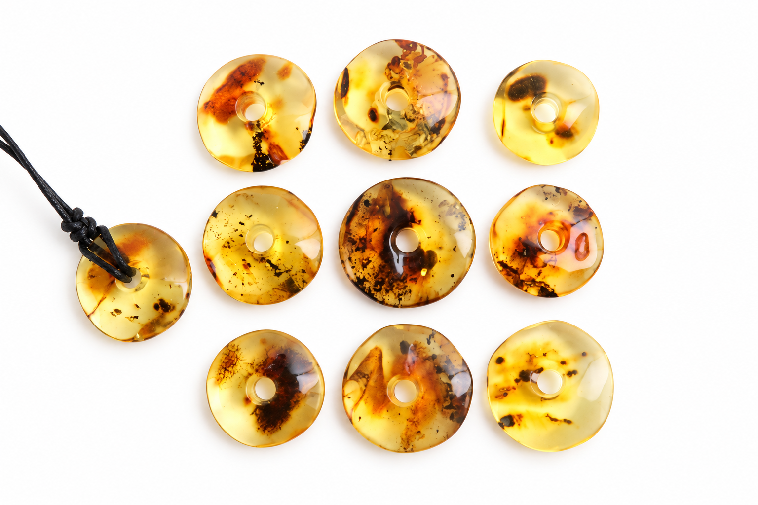 Nine round translucent amber pendants with dark inclusions are arranged on a white background, with one pendant on the left attached to a black cord.