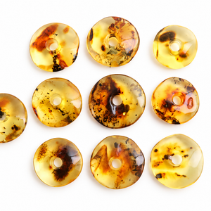 Nine round translucent amber pendants with dark inclusions are arranged on a white background, with one pendant on the left attached to a black cord.