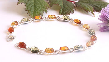 Multicolored beaded bracelet on a white background with green leaves and a purple flower.