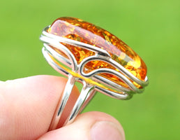 Silver ring with a large amber stone held by a hand against a green background