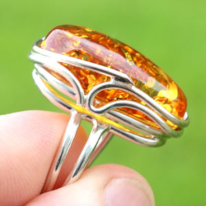 Silver ring with a large amber stone held by a hand against a green background