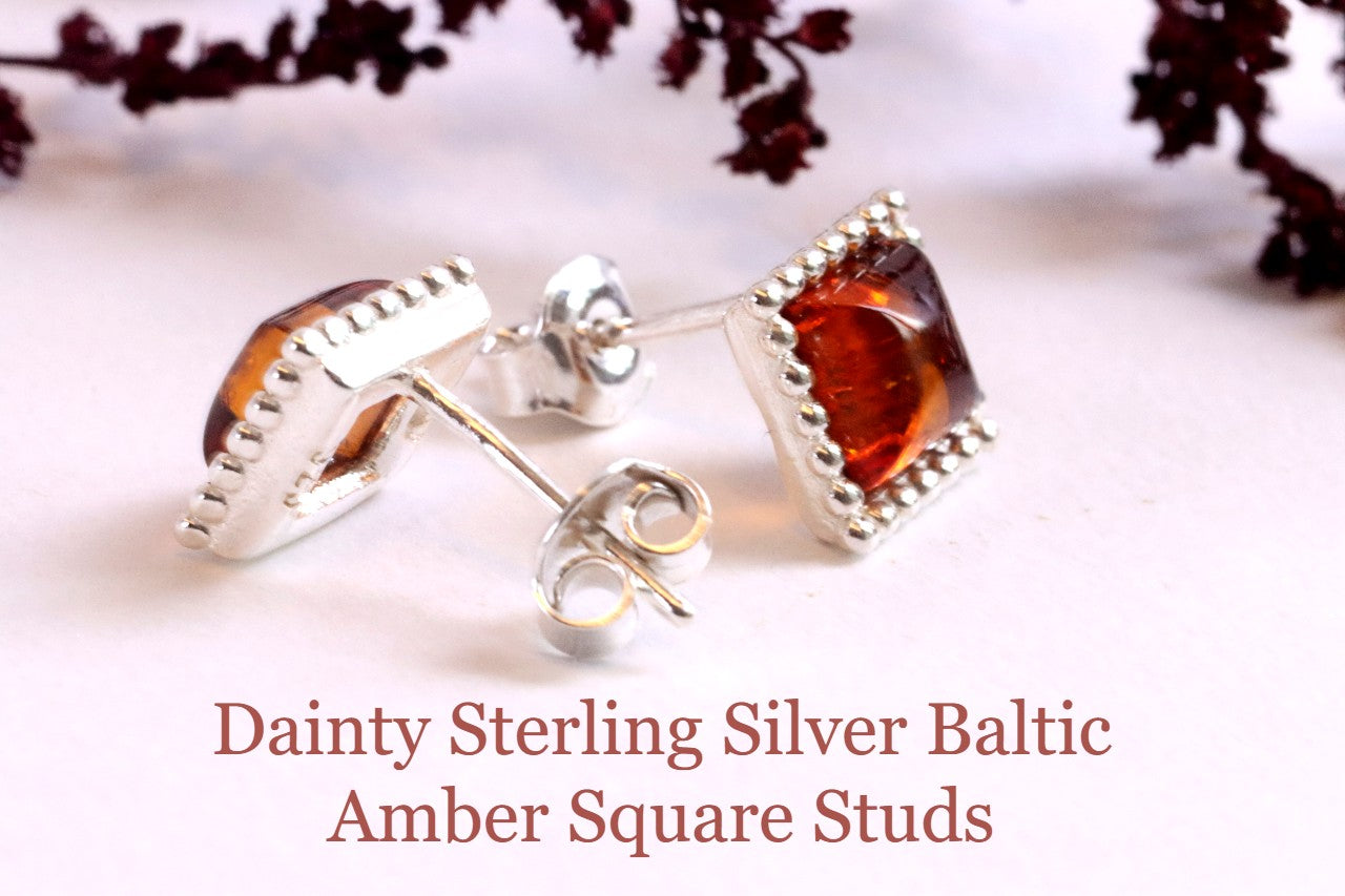 Pair of dainty sterling silver Baltic amber square stud earrings on a light background.