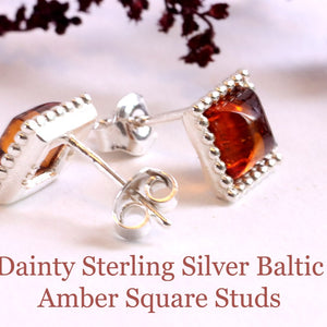 Pair of dainty sterling silver Baltic amber square stud earrings on a light background.