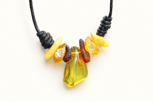 A handmade tumbled stone necklace featuring a large central yellow-green amber bead, flanked by smaller yellow, orange, and brown stones, suspended on a black cord against a white background.