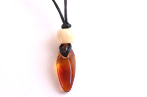 A close-up of a pendant necklace featuring a polished amber-brown teardrop-shaped bead on a black cord, with a small cream-colored spacer bead above it, set against a plain white background.