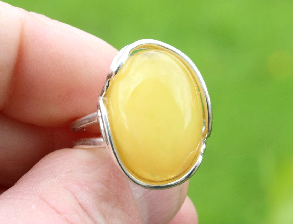 Silver ring with a yellow gemstone held in a hand against a green background