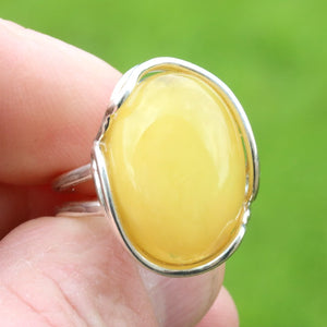 Silver ring with a yellow gemstone held in a hand against a green background