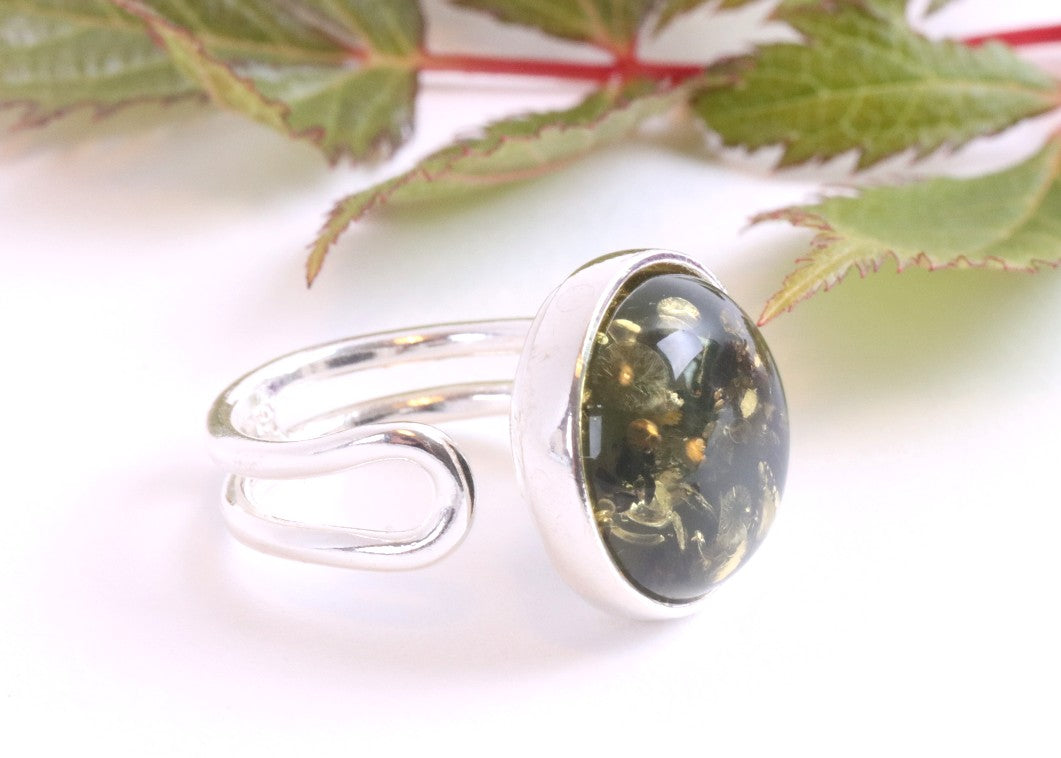 Silver ring with a green gemstone on a white background with leaves.