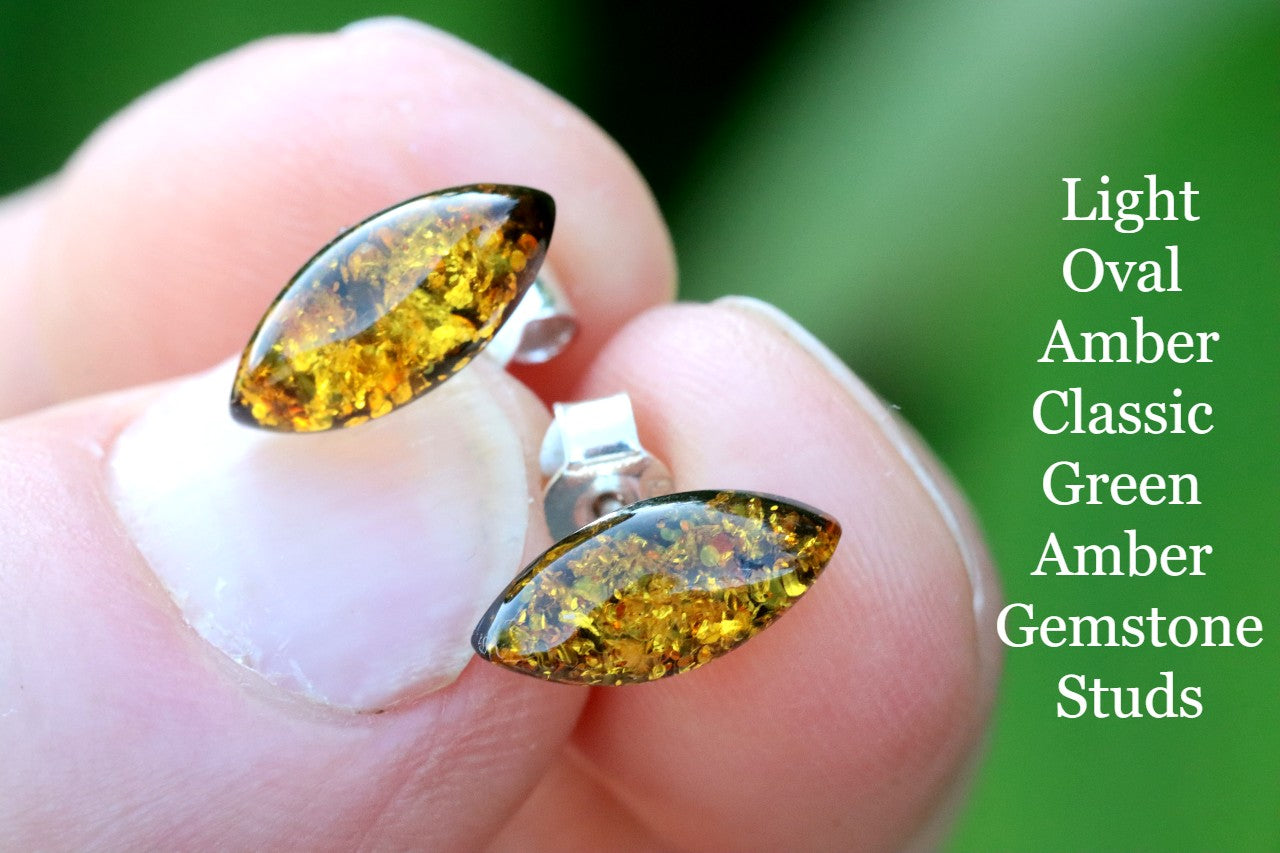 Amber gemstone stud earrings held between fingers with a green background and text description.