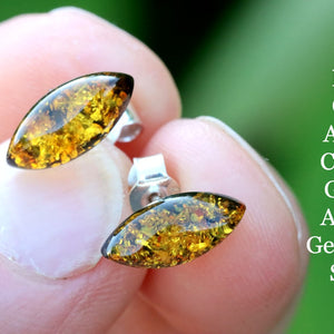 Amber gemstone stud earrings held between fingers with a green background and text description.