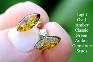 Amber gemstone stud earrings held between fingers with a green background and text description.
