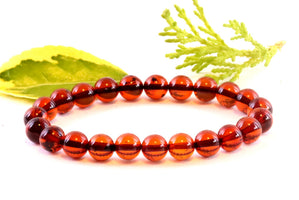 A bracelet made of perfect round red amber beads with a white background and a green leaf in the background.